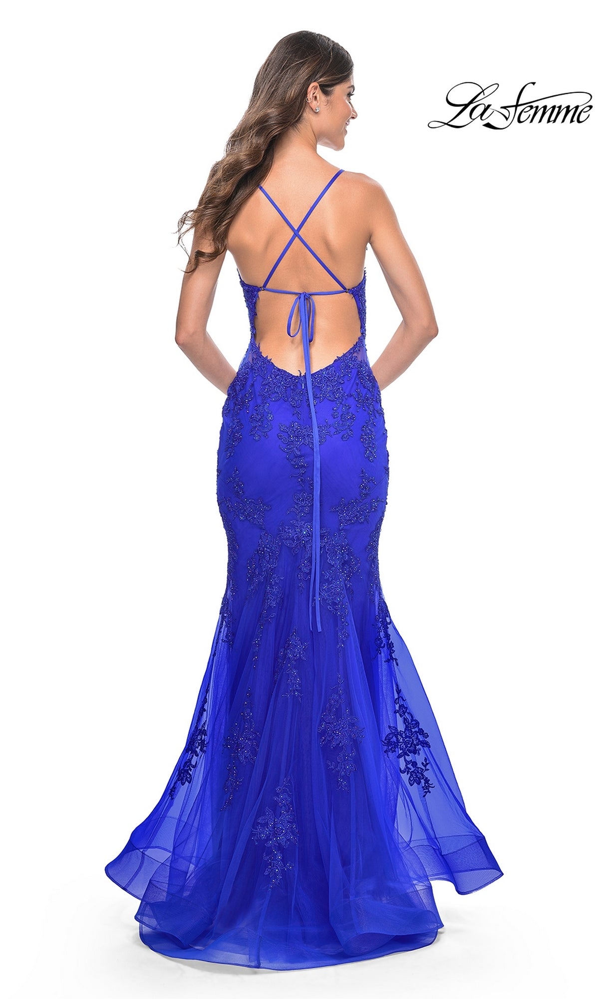 Woman in a fitted, floor-length royal blue La Femme Sheer-Sides Long Mermaid Prom Dress 32305 with beaded lace appliques, open back, and crisscross straps, standing and facing away from the camera.